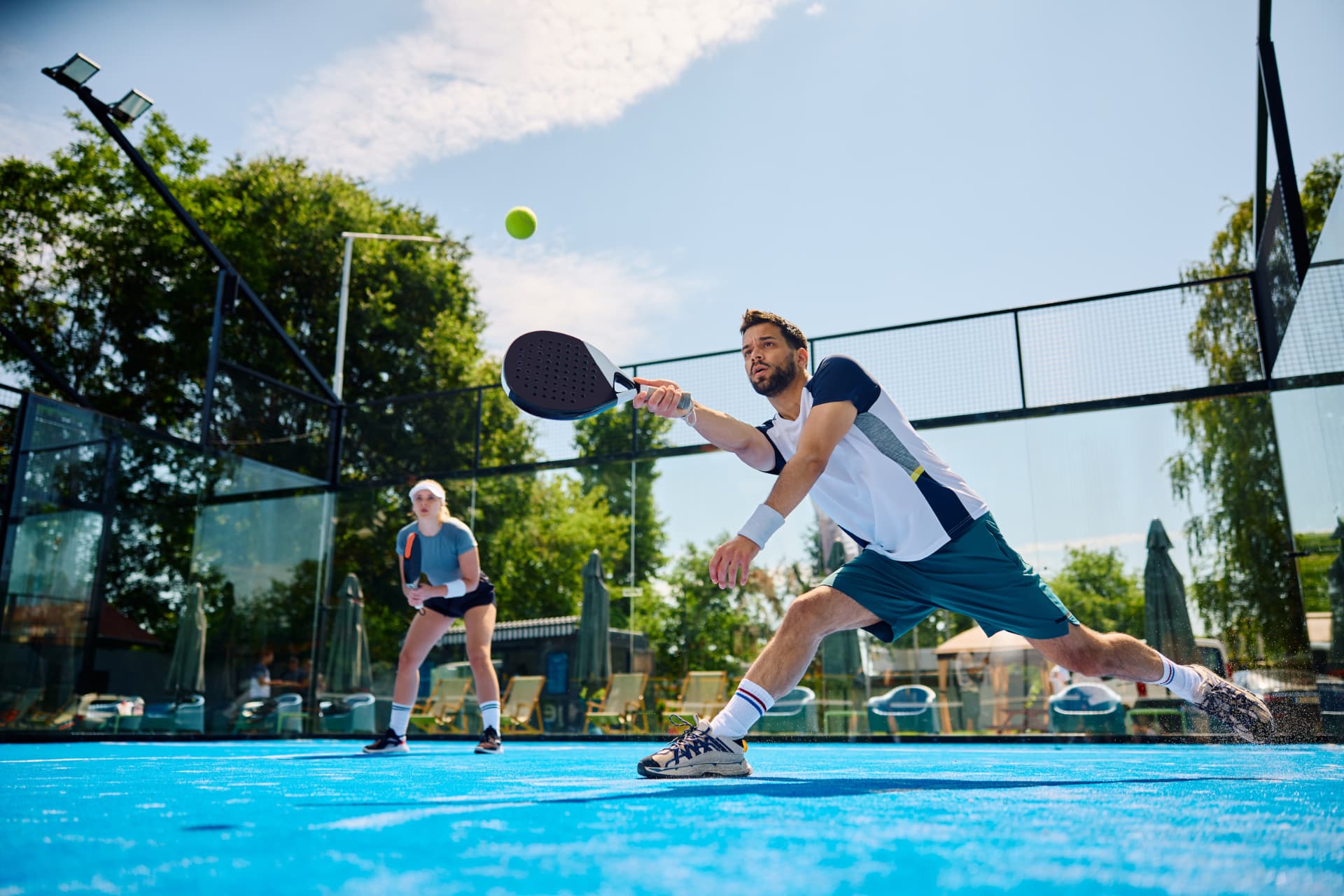 A player lunging to reach the ball on an outdoor court