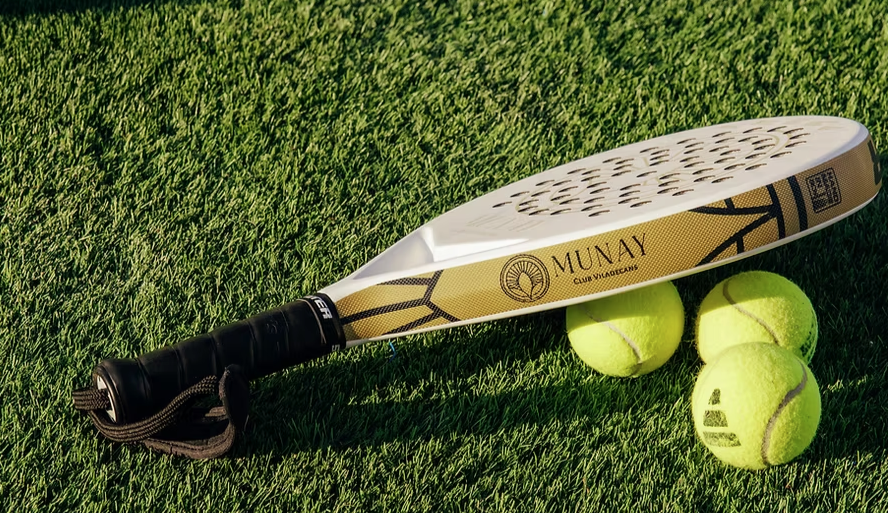 A padel racket and balls resting on the court grass